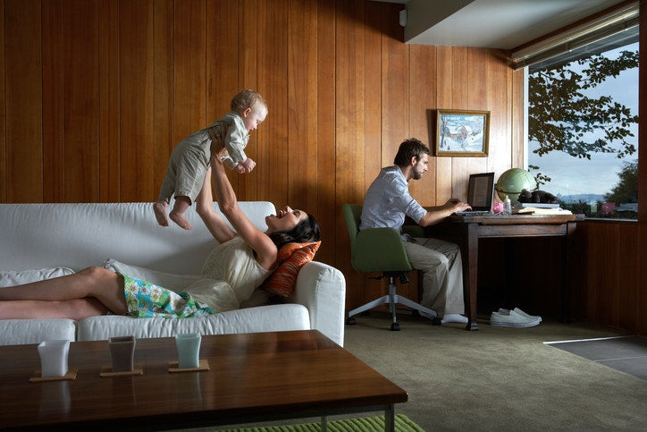 Mother playing with baby girl while father using laptop in living room