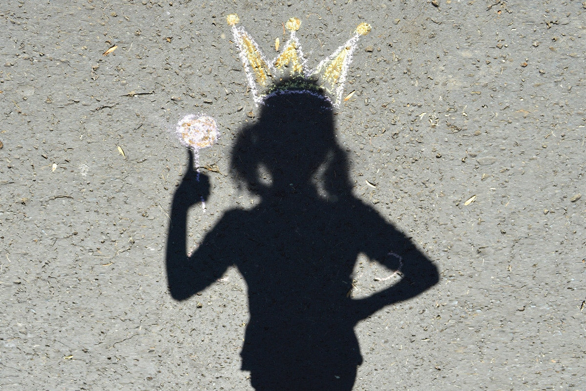 shadow of a girl with a crown and holding lollipop on a road