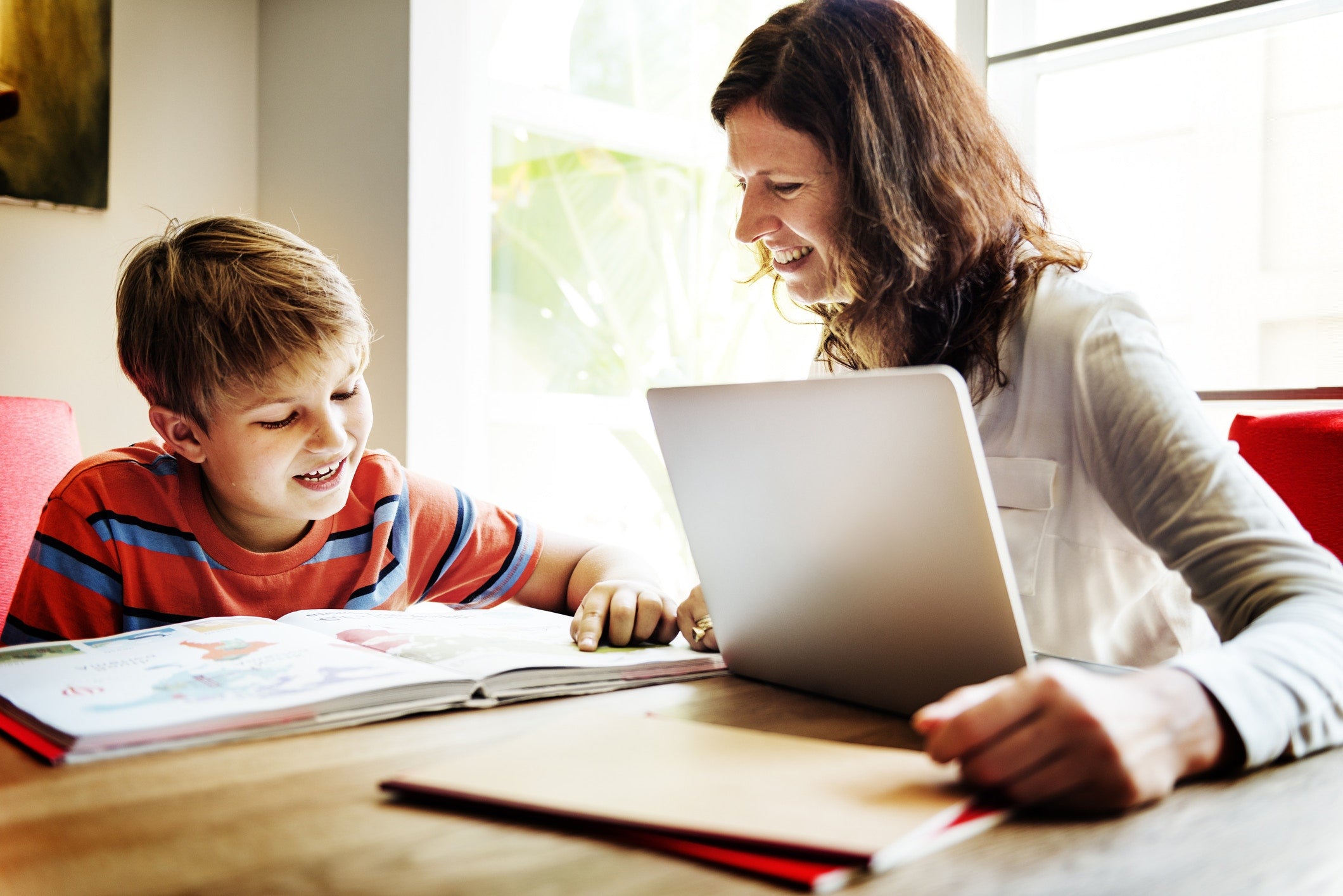 Mother helping son while he is studying and she is working on laptop at home