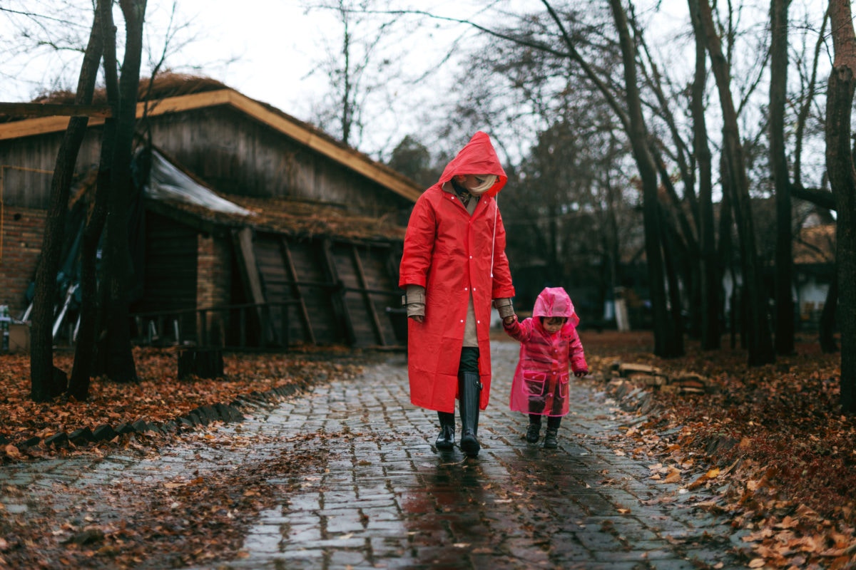 Mother with daughter wearing rain coat and rubber boots walking in a rainy weather