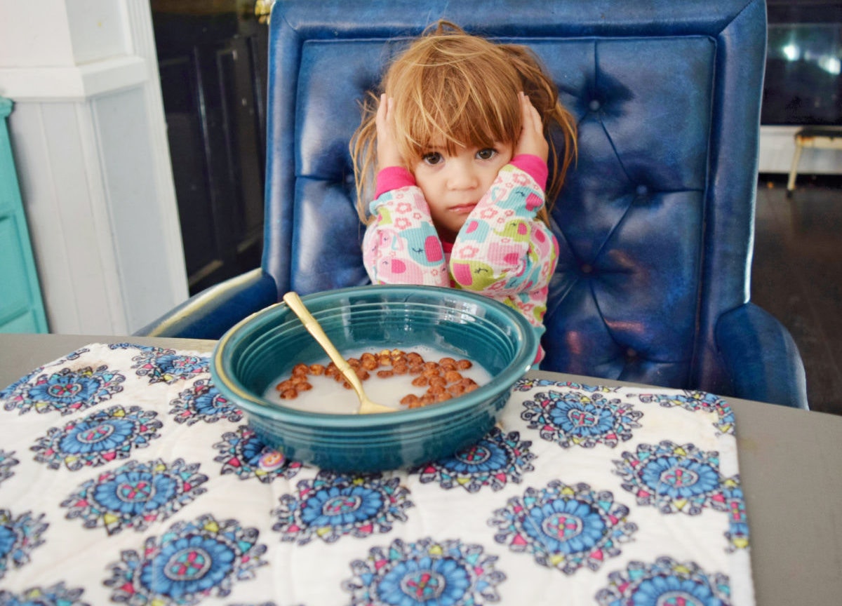 Little girl with annoyed expression sitting at a table with ears covered by her hands