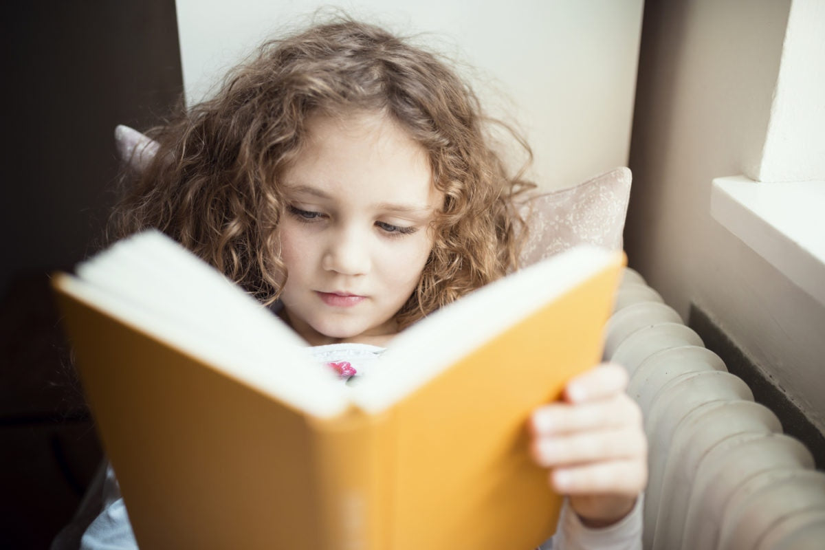 kleines Mädchen mit braunen Haaren liest ein Buch