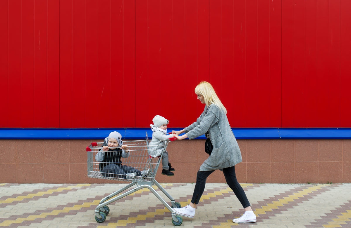 two kids in a shopping cart with a woman pushing the cart