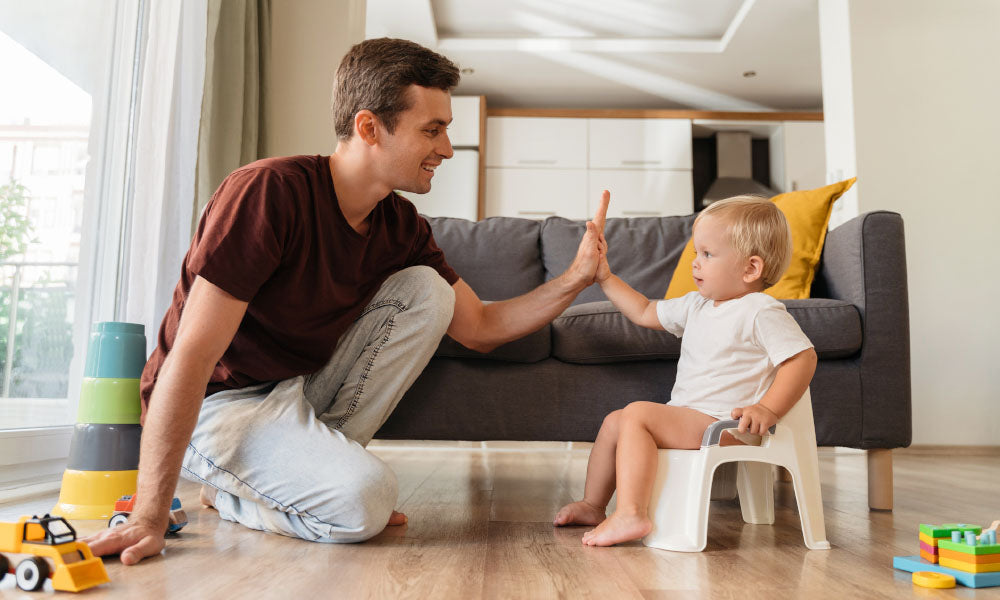 father assisting his little boy sitting on pot