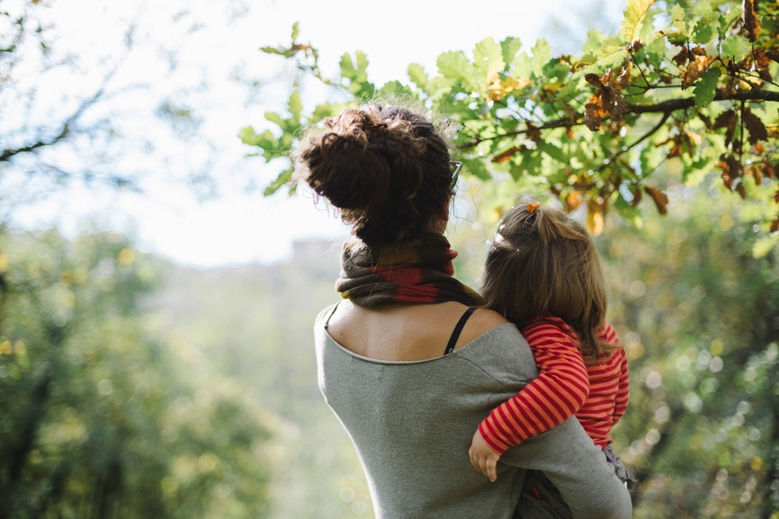 woman holding a baby girl looking at the leaves on trees