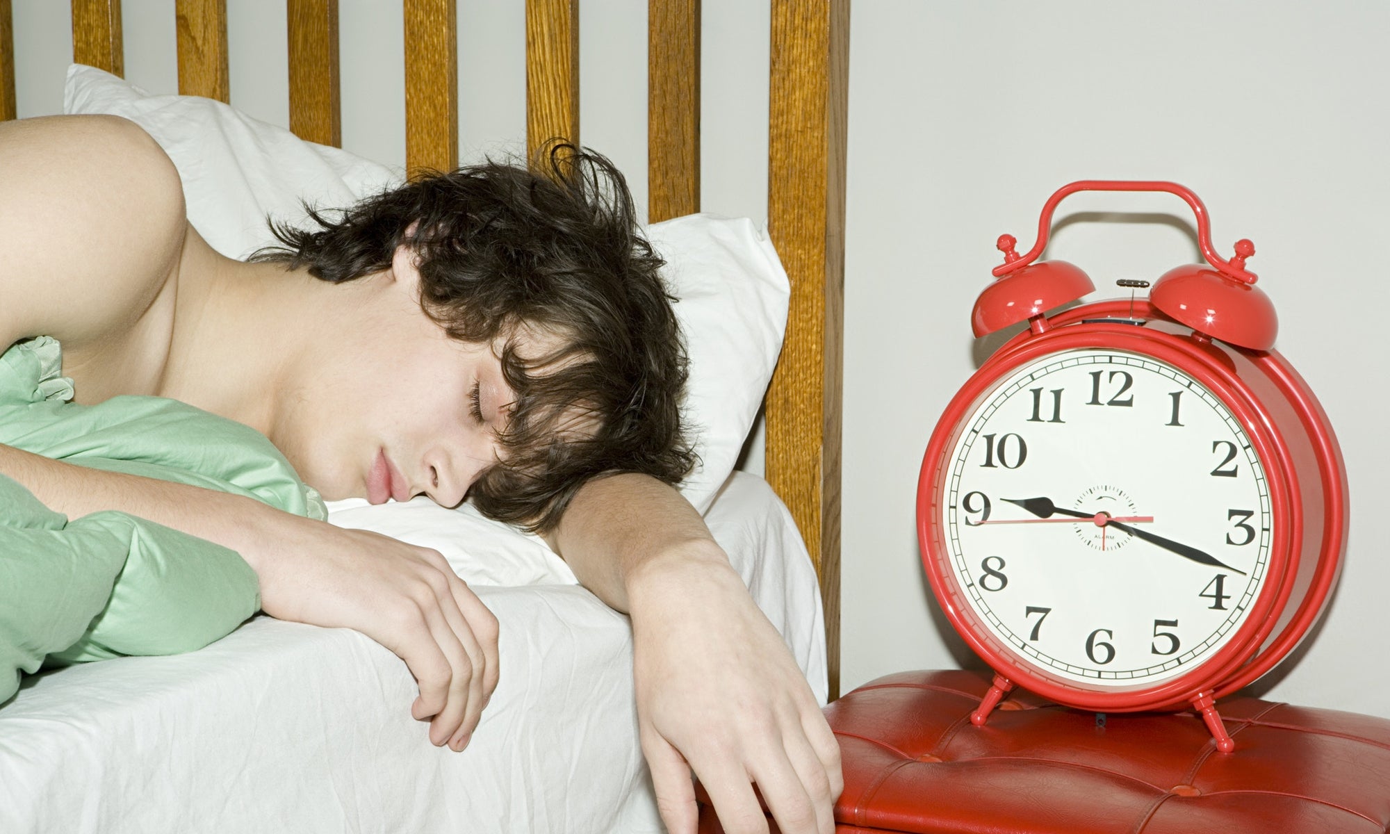 A person sleeping in a bed beside an alarm clock