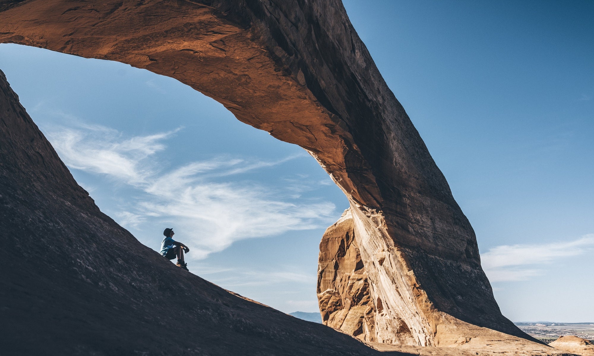 Young man sitting under arched rock