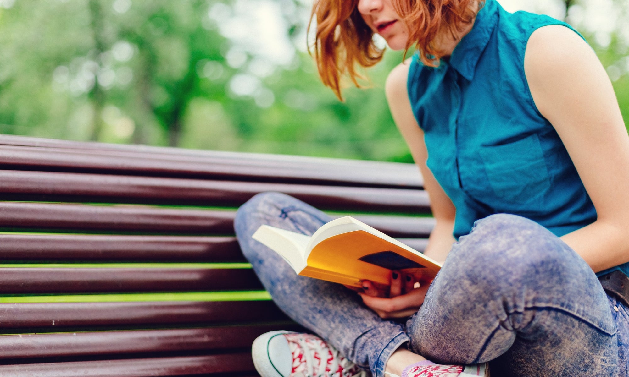 Young woman sitting on a bench in the park and reading book