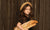 little girl with long brown hair wearing hat and holding loaf of bread