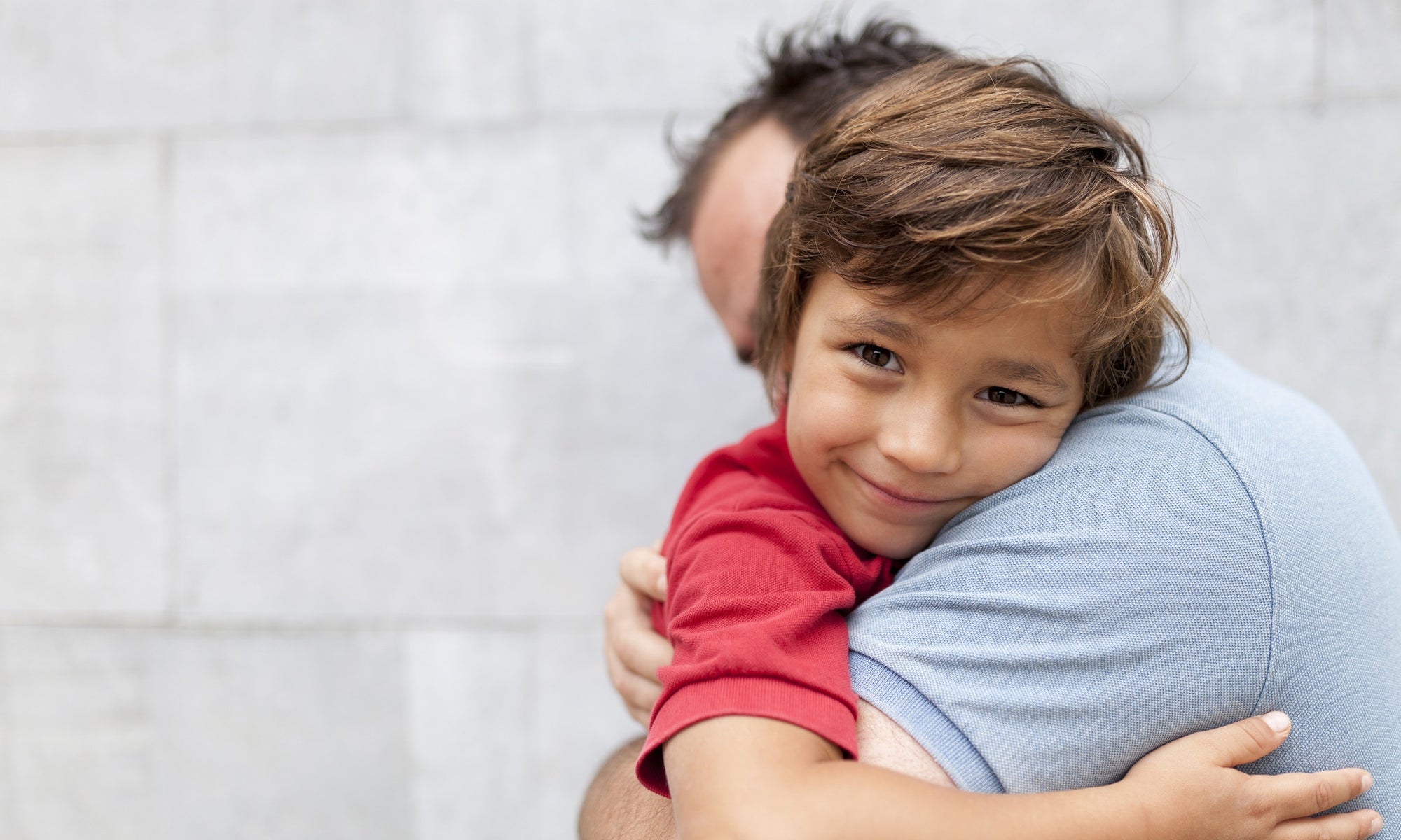 father holding young kid resting on shoulder and smiling