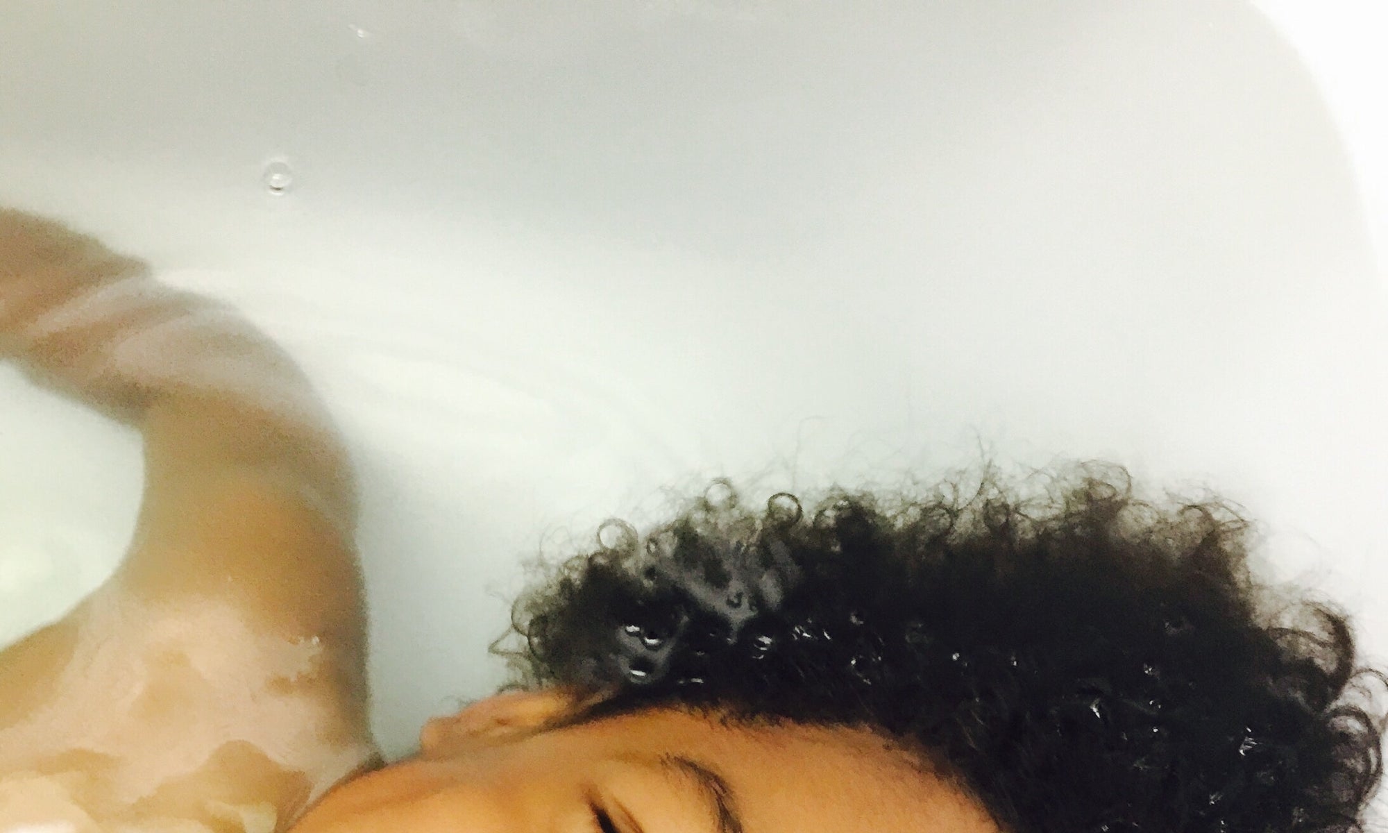 Little Boy with curly hair floating in Bathtub 