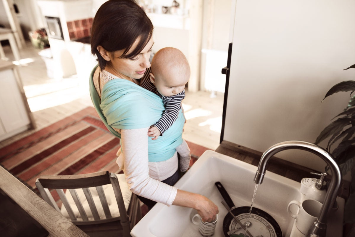 A mother is washing utensils by carrying a kid