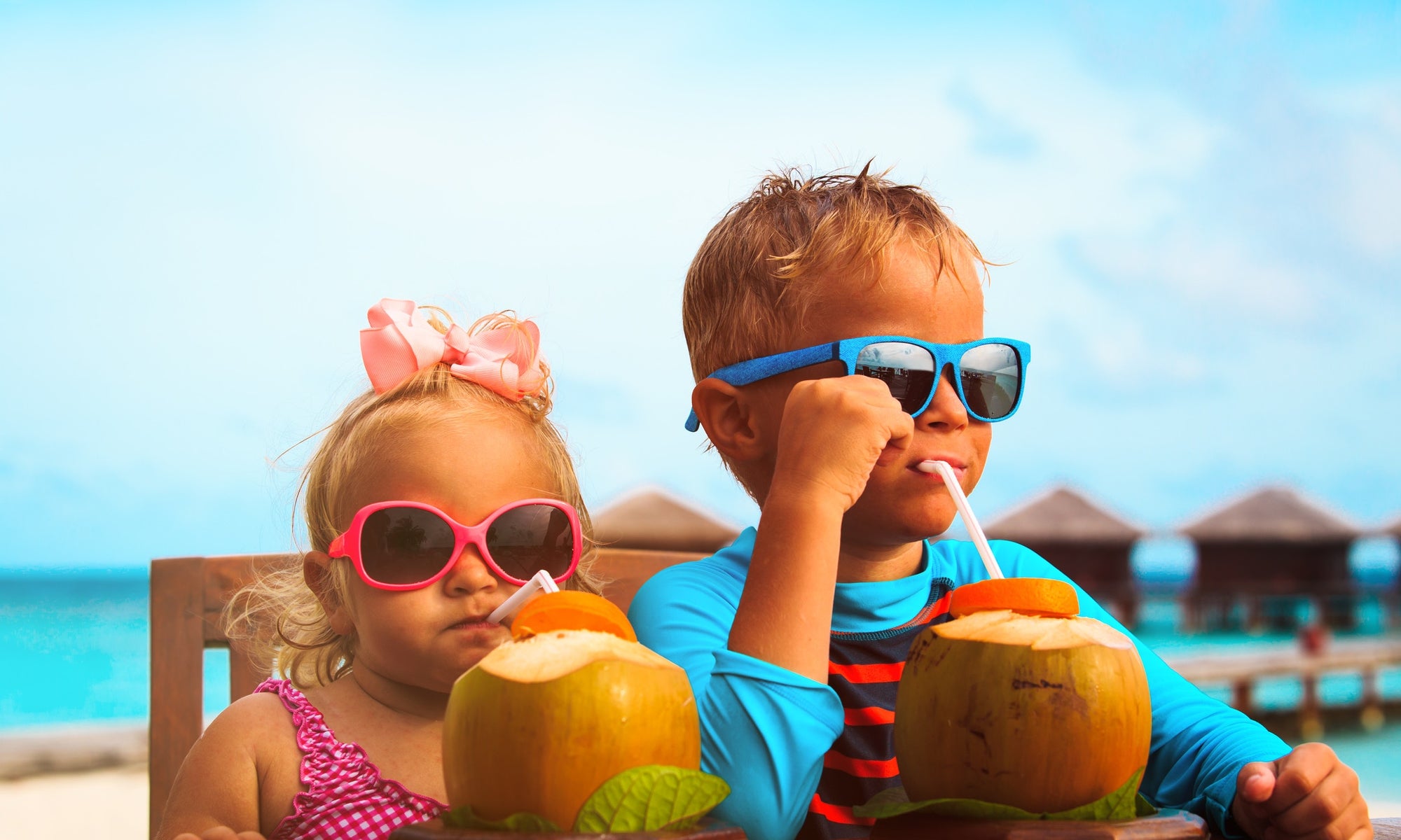 Two children on a table at beach side, wearing googles, drinking coconut water