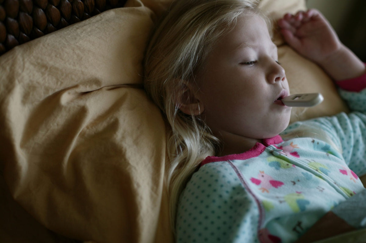 little girl sick in bed with thermometer in mouth