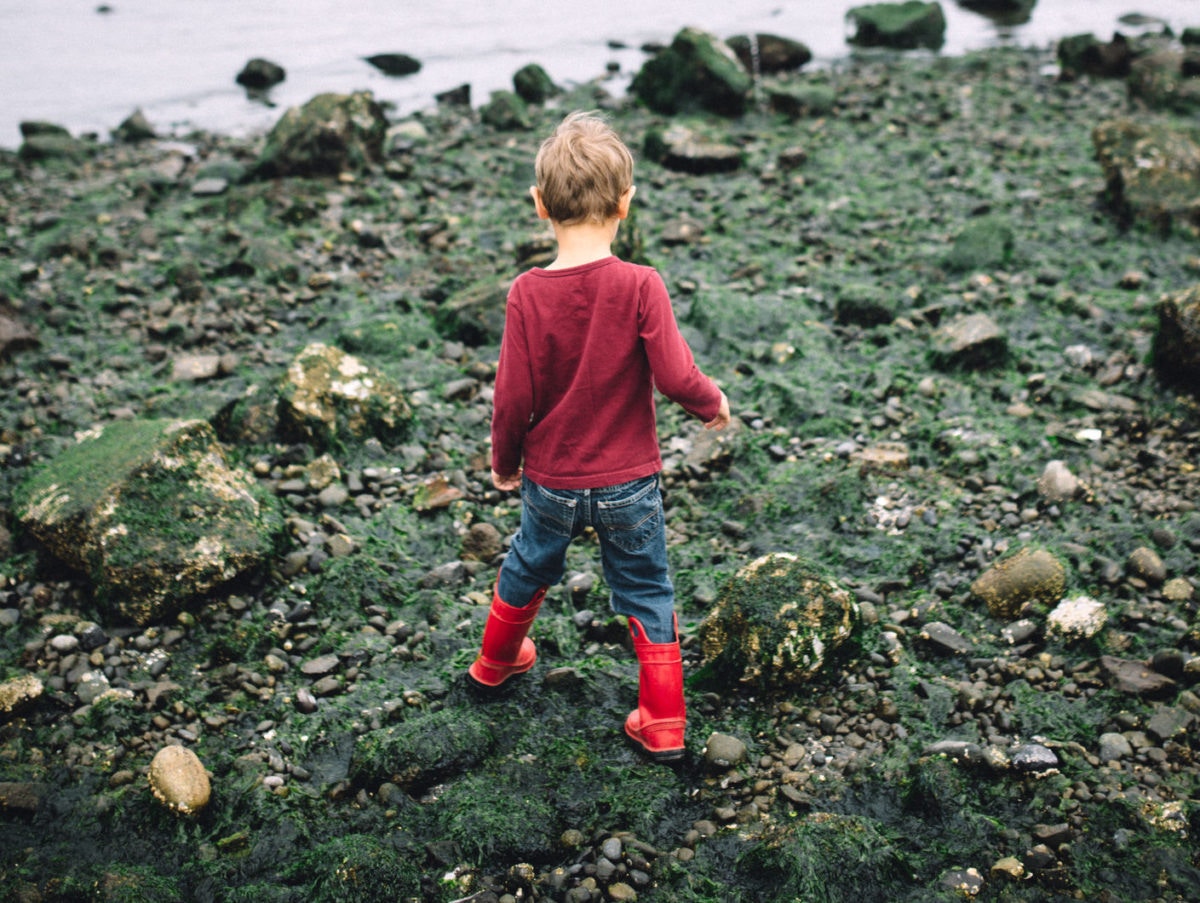 boy with boots walking over rocks towards the sea