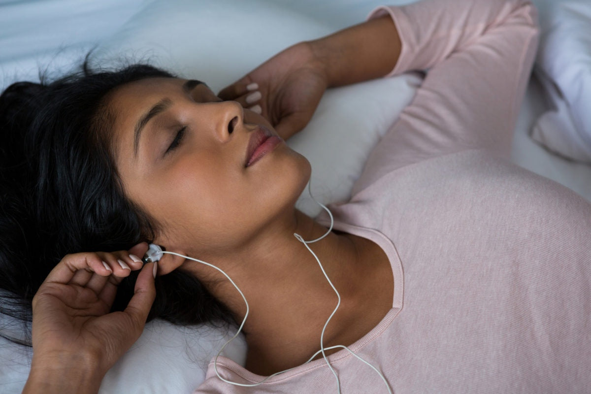 A lady wearing earphone, lying in bed