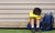 Boy sitting against a wall, backpack by side, looking down