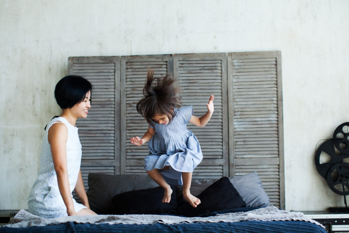 Happy little child girl  jumping on bed and mother looking at her happily