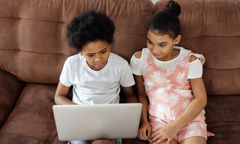Geschwister, die auf einer Couch sitzen und auf einen Computer schauen